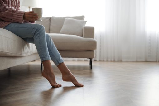 Barefoot woman sitting on sofa in living room, closeup. Floor heating system